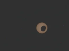 毅力号火星车在火星上观测外星日食2026 年 8 月 19 日当天的太空照片 A yellowish sun against a black background is partially obscured by a Martian moon.