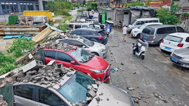 Residents walk past vehicles damaged by a fallen wall in the aftermath of Typhoon Dolphin in eastern China&rsquo;s Zhejiang province. PIC/PTI