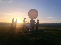 NASA 将利用气球和高空喷气式飞机追逐 8 月 12 日的日全食 People are seen as silhouettes with the sun behind them. They're on a field.