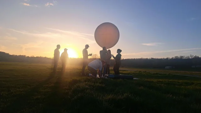 NASA will chase the Aug. 12 total solar eclipse with balloons and a high-altitude jet People are seen as silhouettes with the sun behind them. They're on a field.