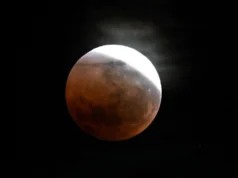 距离 96% 月偏食仅剩 1 周:以下是您需要了解的信息 A photo of a full moon captured during a lunar eclipse in a black sky. Earth's shadow covers the moon, turning it a dull crimson, while a thin crescent is visible to the upper right of the lunar disk.