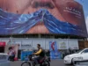 特朗普对伊朗的经济战能否达到空袭和谈判无法达到的效果? Vehicles drive past a billboard with an illustration showing the Strait of Hormuz and the sewn lips of President Trump in a square in downtown Tehran, Iran, May 2.