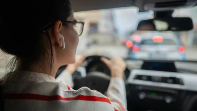 A woman behind the wheel with an earbud in