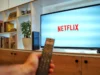 杜比视界已在 Netflix 上推出,但您首先需要这些 – Engadget A remote in hand in the foreground pointed towards a TV on a stand displaying the Netflix logo.