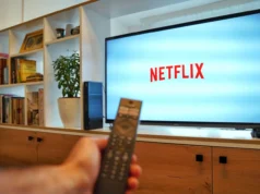 杜比视界已在 Netflix 上推出,但您首先需要这些 – Engadget A remote in hand in the foreground pointed towards a TV on a stand displaying the Netflix logo.