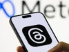 Threads 正在测试播客转录功能 – Engadget Photo of the Threads logo on a smartphone screen with the Meta logo blurred on a white wall in the background.