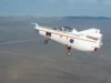 在太空的这一天! 1963 年 8 月 16 日:Wingless M2-F1 完成第一次滑翔飞行 a small white aircraft with a pilot aboard is towed in flight by line extending to the dry lake bed below.