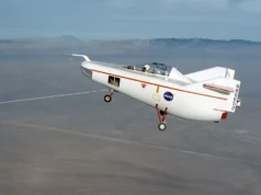 在太空的这一天! 1963 年 8 月 16 日:Wingless M2-F1 完成第一次滑翔飞行 a small white aircraft with a pilot aboard is towed in flight by line extending to the dry lake bed below.