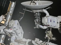 宇航员修复国际空间站创造历史2026 年 8 月 25 日当天的太空照片 two astronauts in bulky white space suits maneuver on the outside of a large facility covered in solar panels and machinery